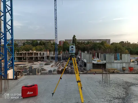 Тотална станция на тринога върху плочата, сградата на Royal Garden 3 в груб строеж отзад, 07.09.2024